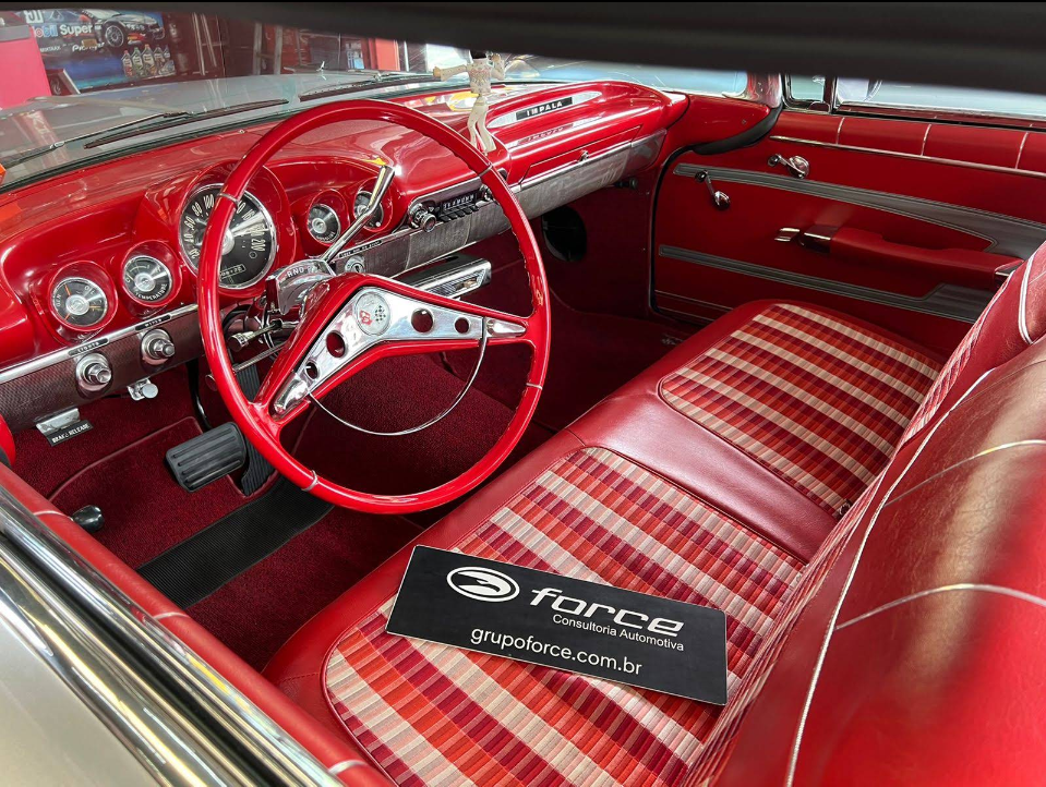 Interior clássico de automóvel restaurado com bancos em vinil vermelho e xadrez, painel e volante vermelhos com detalhes cromados, placa da Force Consultoria Automotiva sobre o banco, ambiente de oficina especializada, fotografia realista